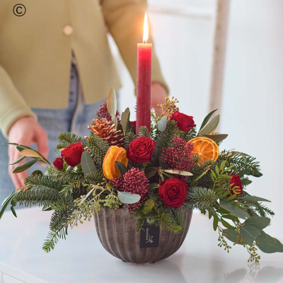 Classic Christmas Candle Arrangement - A quick rundown: a gorgeous selected of fresh festive flowers, arranged by a florist around a red candle, in a dark copper coloured ceramic bowl.

Colour & style: festive favourites. Rich reds, burgundies and greens. Pops of cream and peach. You might see coppery painted pinecones, scented dried fruit, spruce and pine.

A great gift for: helping to deck their halls (or their Christmas table), lovers of a cosy Christmas.

All the other details:
• This will be handcrafted by a Dingles Florist, who will use all their care and skill and make sure it arrives ready to wow.
• It won't include any lilies.
• It might not look exactly like the pictures because each arrangement is bespoke, made by hand.
• It's guaranteed to look gorgeous for at least 7 days, or we'll put it right.
• It could feature buds, but they'll open up quickly.
• The packaging is all recyclable or biodegradable.
• It comes with a lovely card, the florist will add your message inside by hand.

Legal bits:
Warning:- Do not leave burning candles unattended and always place on a protected surface. Keep out of reach of children and pets.