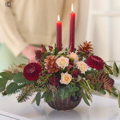 Signature Christmas Candle Arrangement - A quick rundown: a large candle arrangement – stunning festive flowers arranged by a Dingles Florist around red candles, in a dark copper coloured ceramic bowl.

Colour & style: festive favourites. Rich reds, burgundies and greens. Pops of cream and peach. You might see coppery painted pinecones, scented dried fruit, spruce and pine.

A great gift for: dressing the Christmas table, fans of cosy Christmas style, lovers of festive tradition.

All the other details:
• This will be handcrafted by a Dingles Florist, who will use all their care and skill and make sure it arrives ready to wow.
• It won't include any lilies.
• It might not look exactly like the pictures because each arrangement is bespoke, made by hand.
• It's guaranteed to look gorgeous for at least 7 days, or we'll put it right.
• It could feature buds, but they'll open up quickly.
• The packaging is all recyclable or biodegradable.
• It comes with a lovely card, the florist will add your message inside by hand.

Legal bits:
Warning:- Do not leave burning candles unattended and always place on a protected surface. Keep out of reach of children and pets.