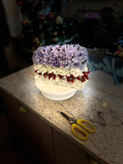 3d Cake - A unique and eye-catching 3D cake slice floral arrangement, expertly crafted to resemble a realistic slice of cake using fresh flowers. Designed with layers in delicate lilac and creamy white tones, this piece is beautifully finished with a band of vibrant red berries to add texture and contrast.

Created using Oasis Renewal foam, this design not only provides excellent hydration for the flowers but also supports a more sustainable approach to floral design.