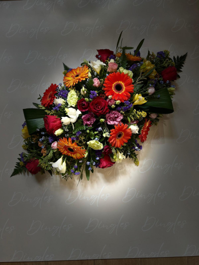 Vibrant Funeral Tribute Arrangement - A striking and uplifting funeral tribute arrangement, beautifully designed with a vibrant mix of fresh flowers in rich, bold colours. This piece features eye-catching gerberas, classic roses, and complementary seasonal blooms in shades of red, orange, white, and purple, all enhanced with lush green foliage.

Arranged in a full, flowing style, this tribute offers a warm and expressive way to celebrate the life of a loved one. The bright colour palette provides a more cheerful and celebratory tone, reflecting cherished memories, personality, and love.